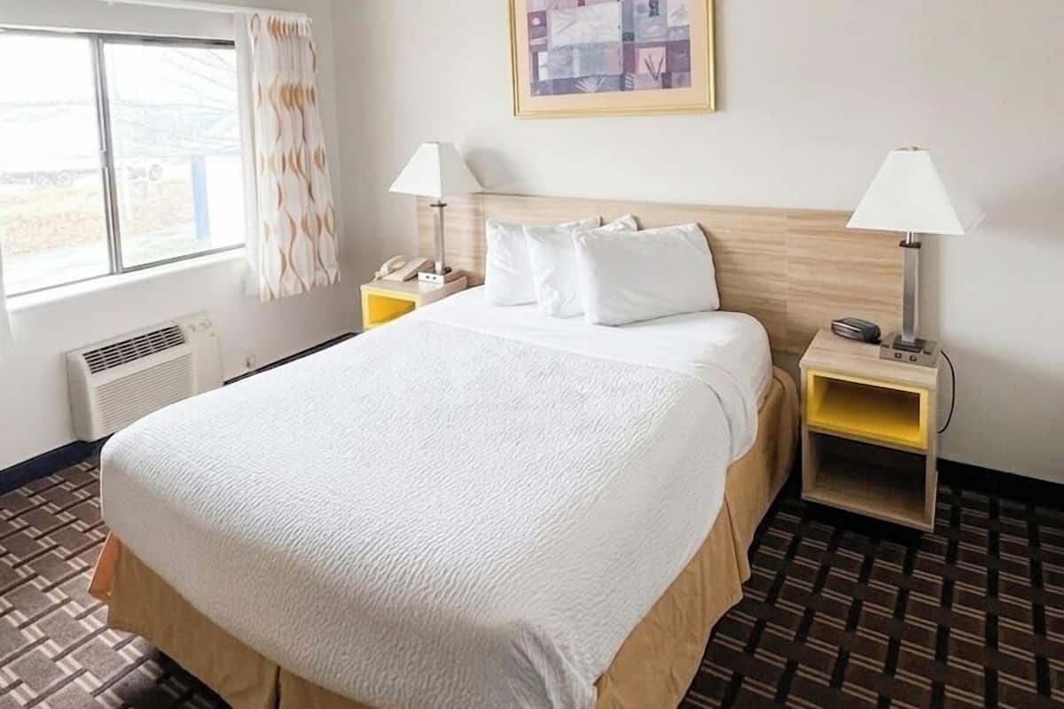 A hotel room with a large bed, two bedside tables, a window with curtains, a radiator, and a framed picture on the wall.