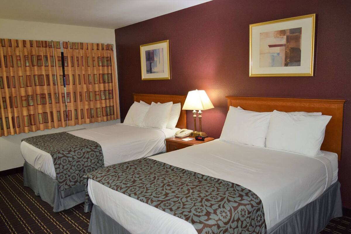 A hotel room with two beds, a nightstand with a lamp, and two framed pictures on the wall.