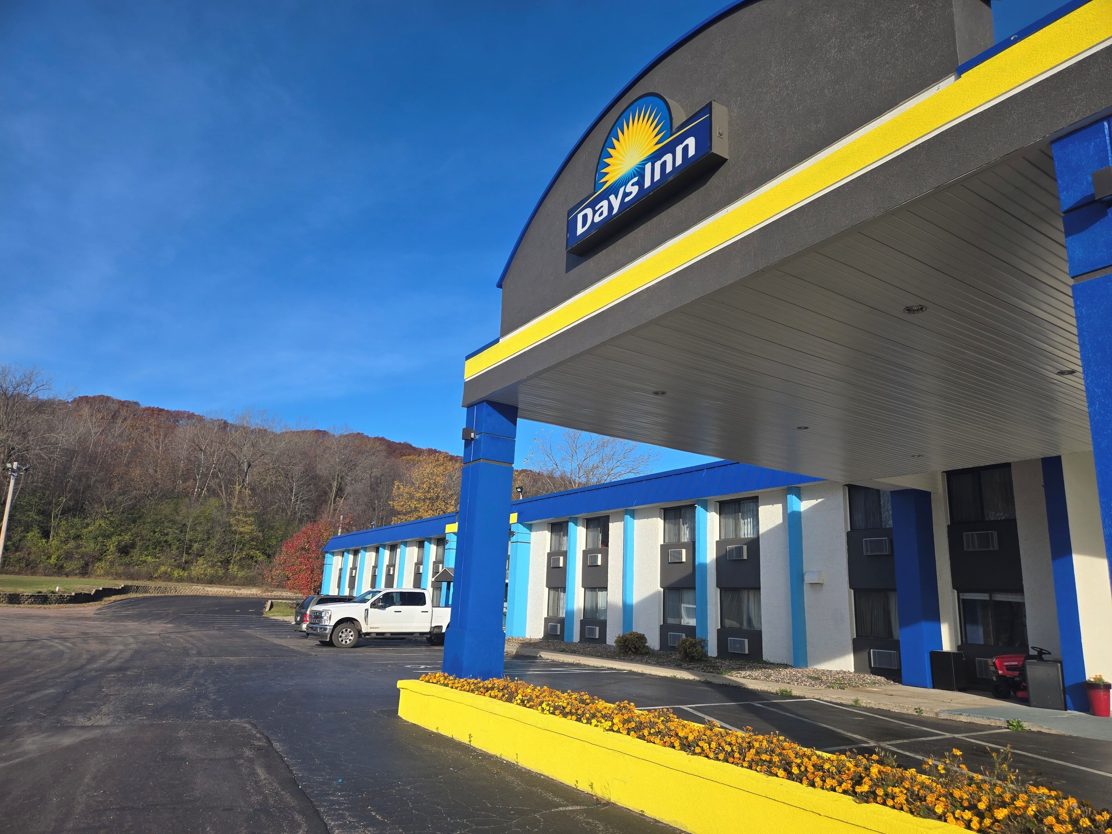 Un Days Inn con fachada azul y blanca, un dosel de estación de servicio y un estacionamiento con una camioneta blanca.