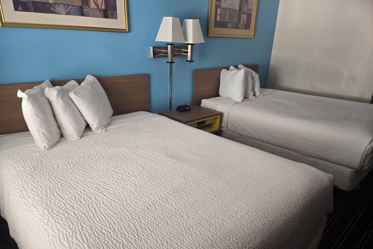 A hotel room with two beds, a nightstand, a lamp, and framed pictures on the wall.