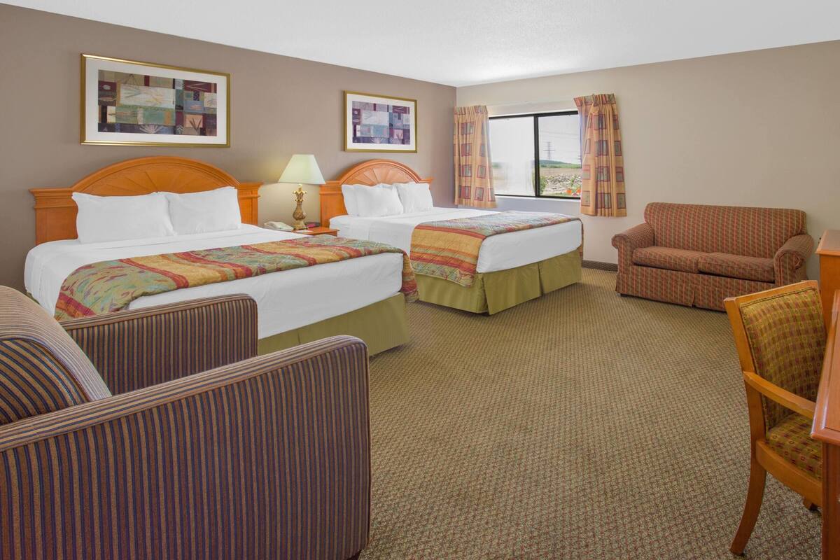 A hotel room with two beds, a sofa, a chair, and a large window with curtains.