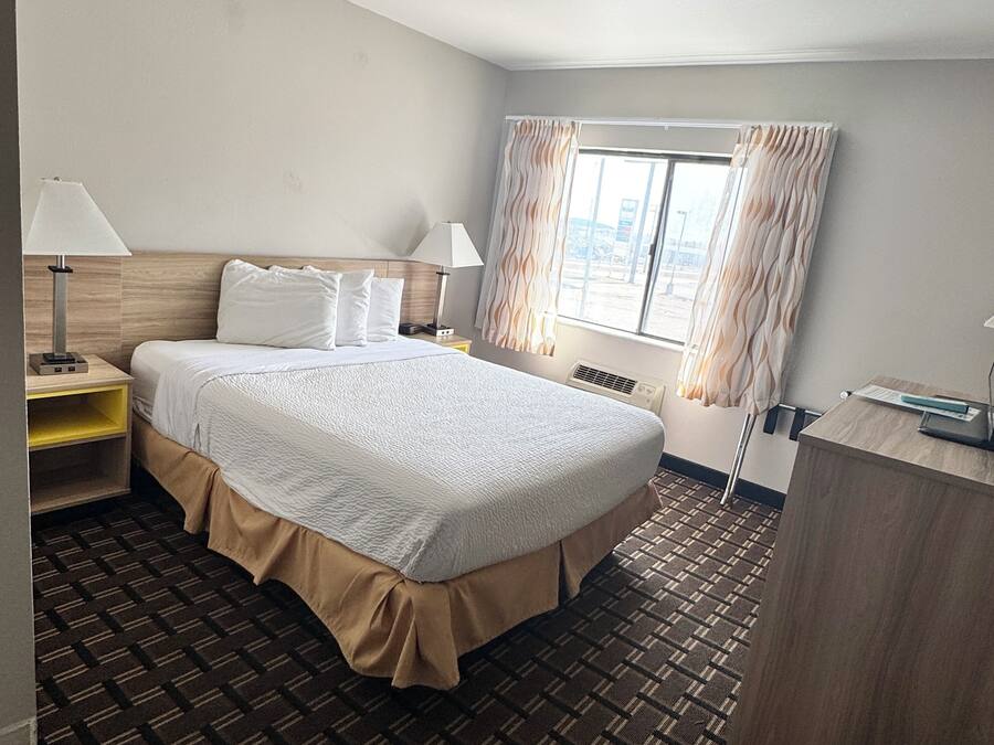 Ein Hotelzimmer mit einem Bett, Nachttischen, einem Schreibtisch, einem Fenster mit Vorhängen und einem gemusterten Teppich.
