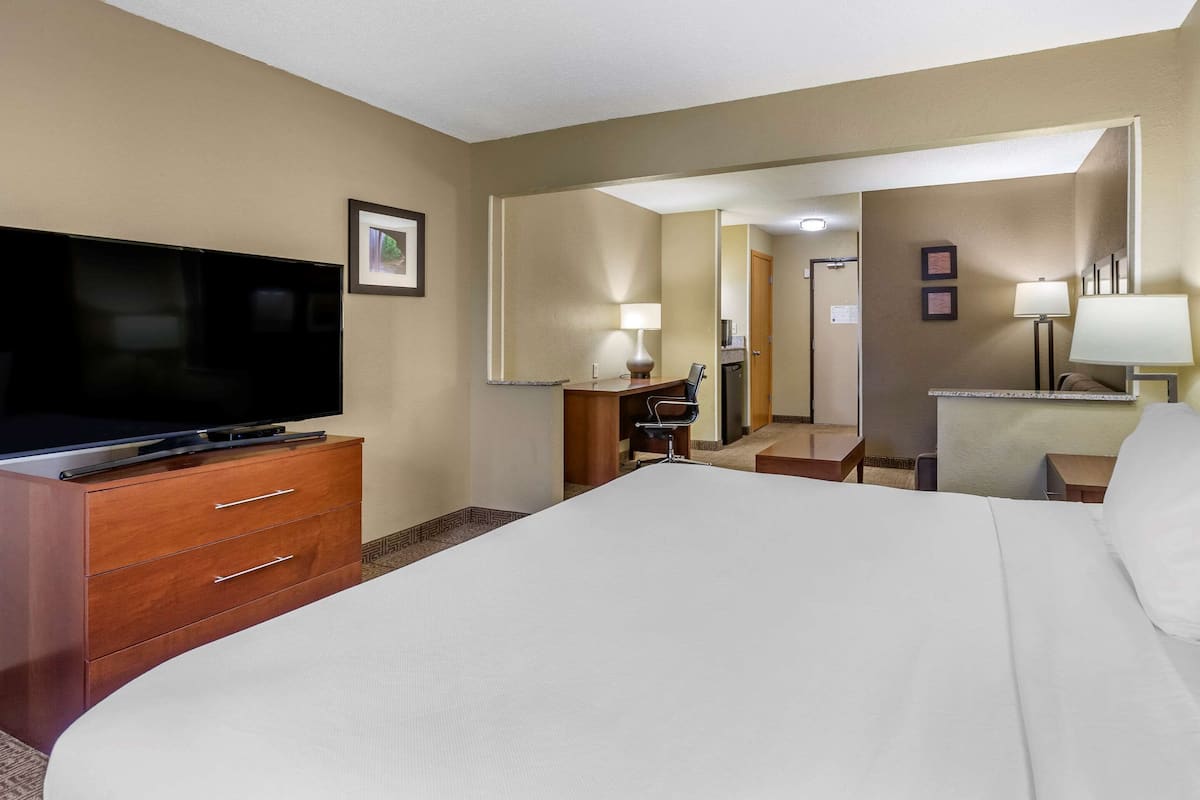 A hotel room with a large bed, a TV on a wooden dresser, a desk with a chair, and a mirror.
