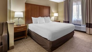 Quarto de hotel com uma cama grande, duas mesas de cabeceira, uma escrivaninha, uma cadeira e uma janela com cortinas.