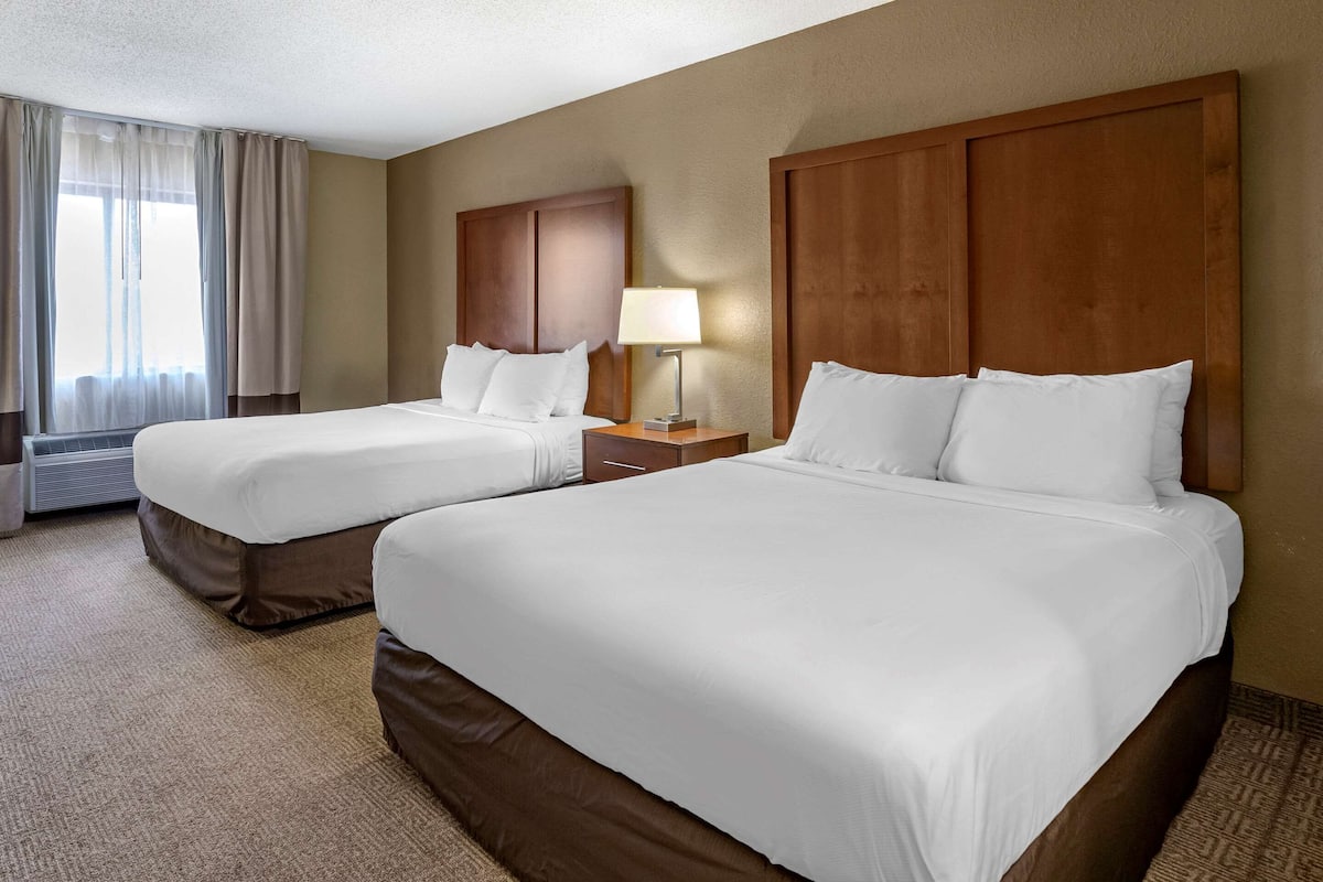 A hotel room with two beds, a nightstand with a lamp, and a window with curtains.