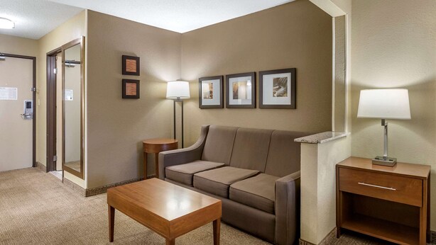 Quarto de hotel com sofá, mesa de madeira, luminária e quadros nas paredes.