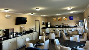 Uma sala de jantar de hotel com várias mesas e cadeiras, uma máquina de café e uma geladeira.