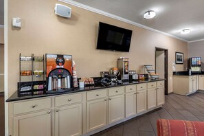 Cocina de hotel con estación de café, televisor montado en la pared y zona de kitchenette.