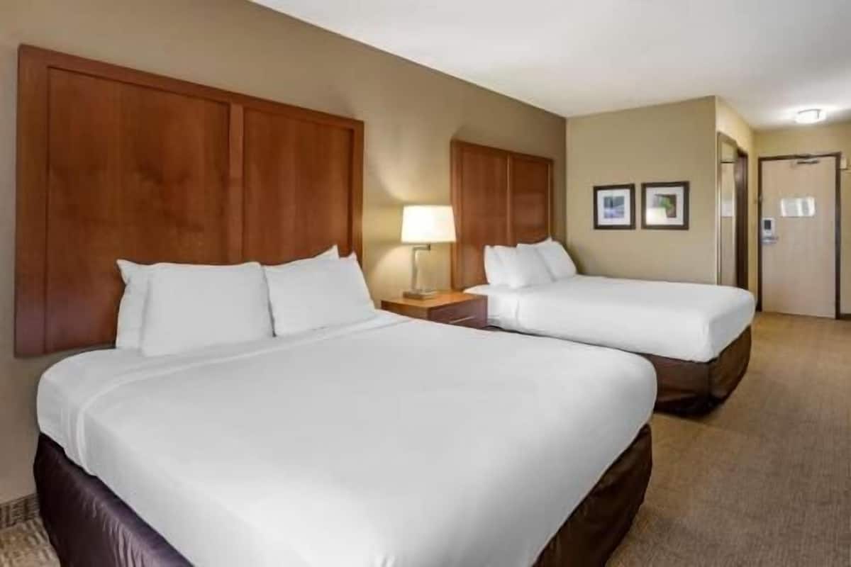 Two beds with wooden headboards, a nightstand with a lamp, and a door with a sign.