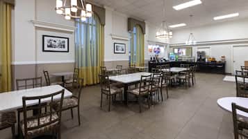 A restaurant with multiple tables and chairs, a counter with a coffee machine, and framed pictures on the walls.