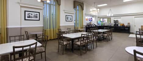 Ein Restaurant mit mehreren Tischen und Stühlen, einer Theke mit einer Kaffeemaschine und gerahmten Bildern an den Wänden.
