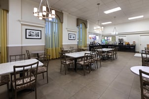 Un restaurante con varias mesas y sillas, una barra con máquina de café y cuadros en las paredes.
