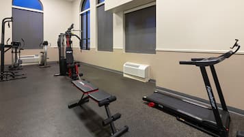 Un gimnasio con equipo de ejercicio, incluyendo una banca, cinta de correr y máquinas de pesas.