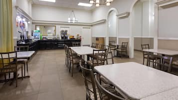 A spacious dining area with multiple tables and chairs, a coffee station, and a counter with various food items.