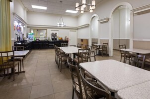 Un comedor amplio con varias mesas y sillas, una estación de café y una barra con diferentes opciones de comida.