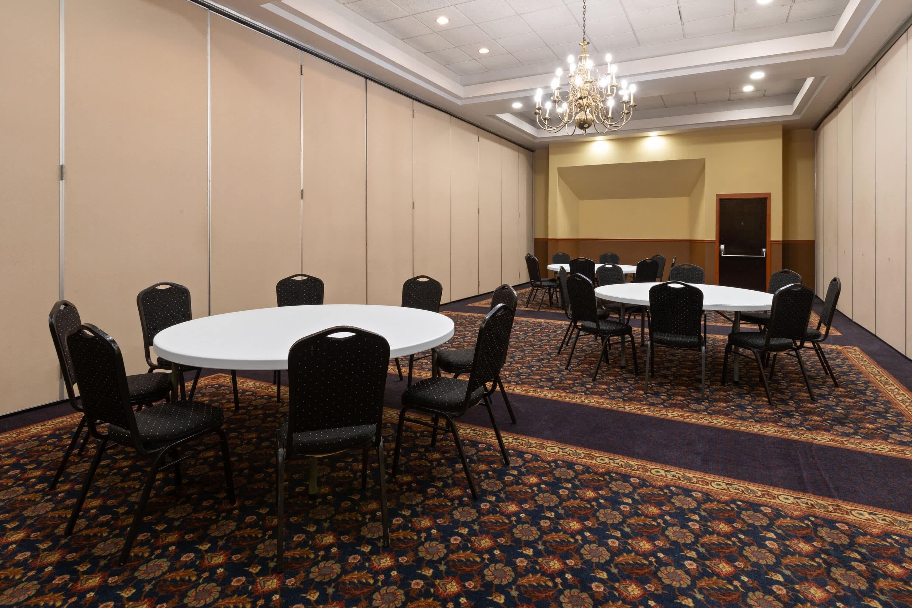 A conference room with round tables and chairs, a patterned carpet, and a chandelier.