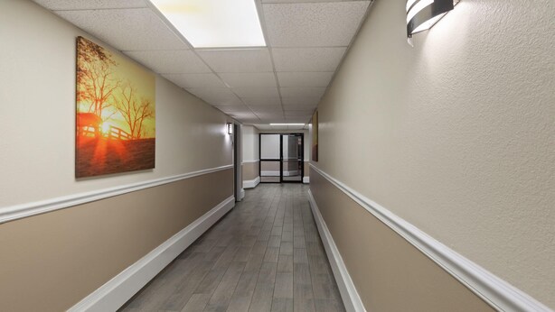 A corridor with a wooden floor, beige walls, and a painting on the left. - Baymont by Wyndham Festus (Festus)