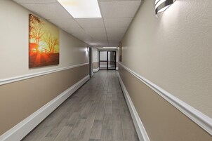 A corridor with a wooden floor, beige walls, and a painting on the left.