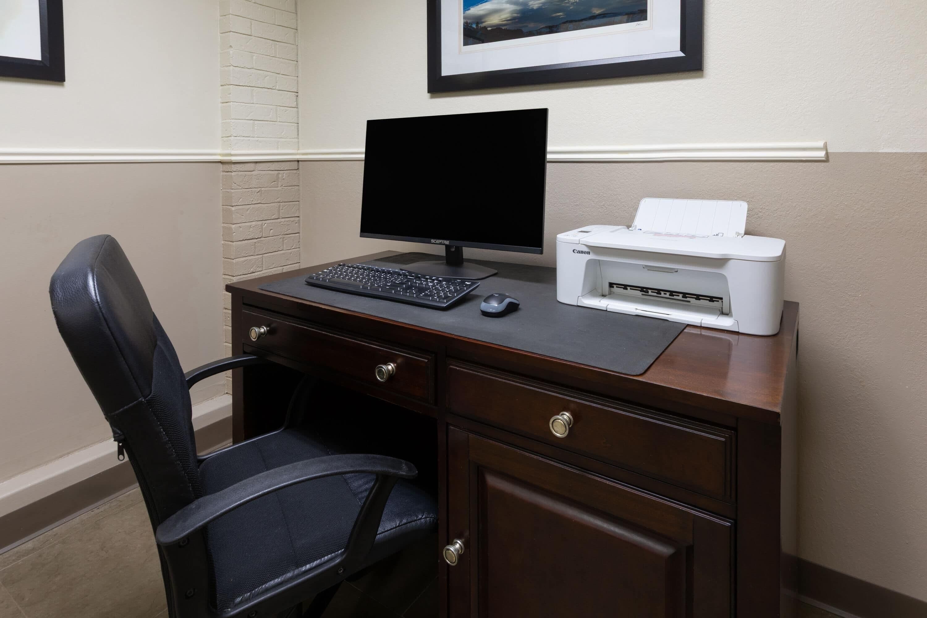 A dark wood desk with a black monitor, a keyboard, a mouse, and a Canon printer.