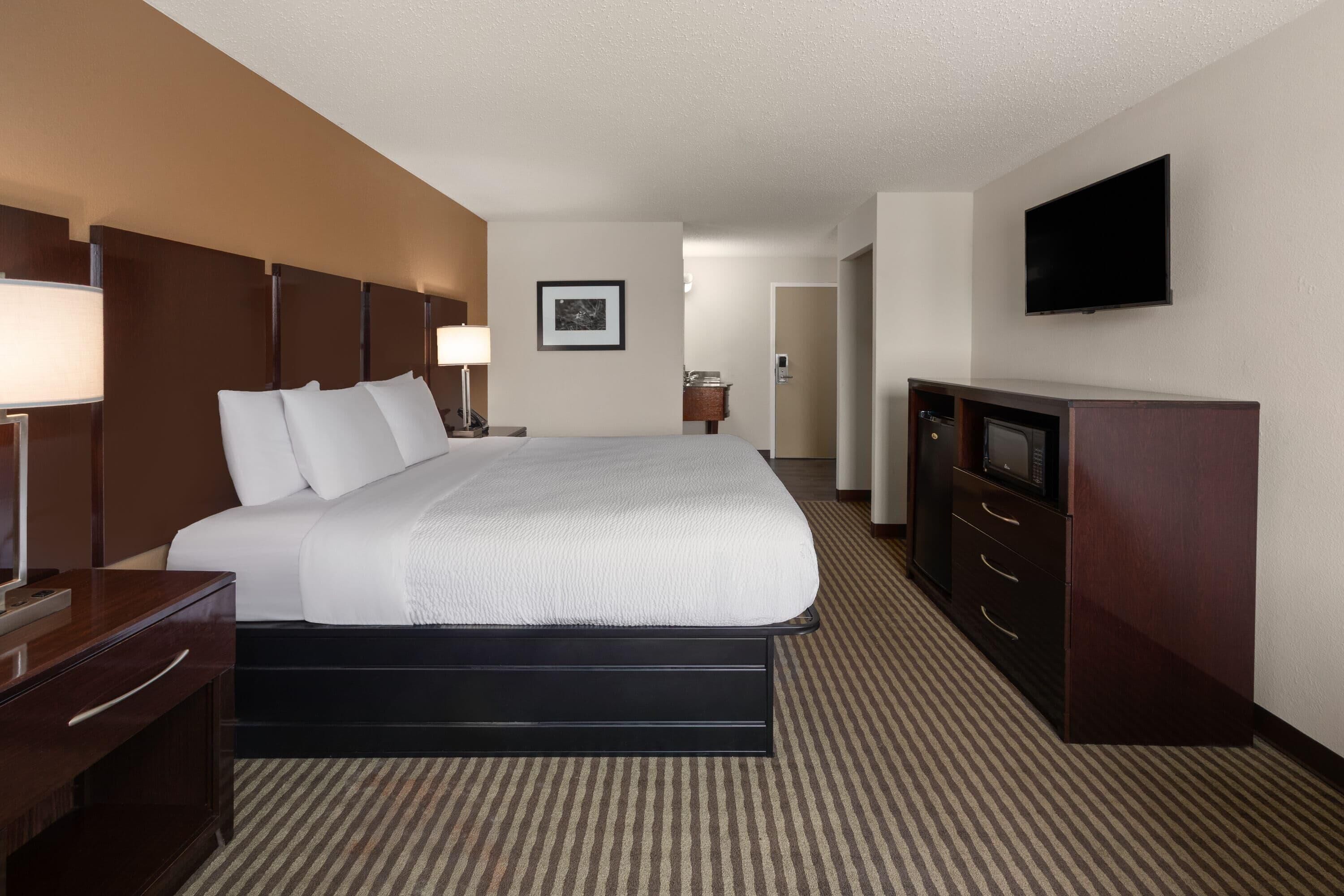 A hotel room with a large bed, a desk, a television, and a door leading to a bathroom.