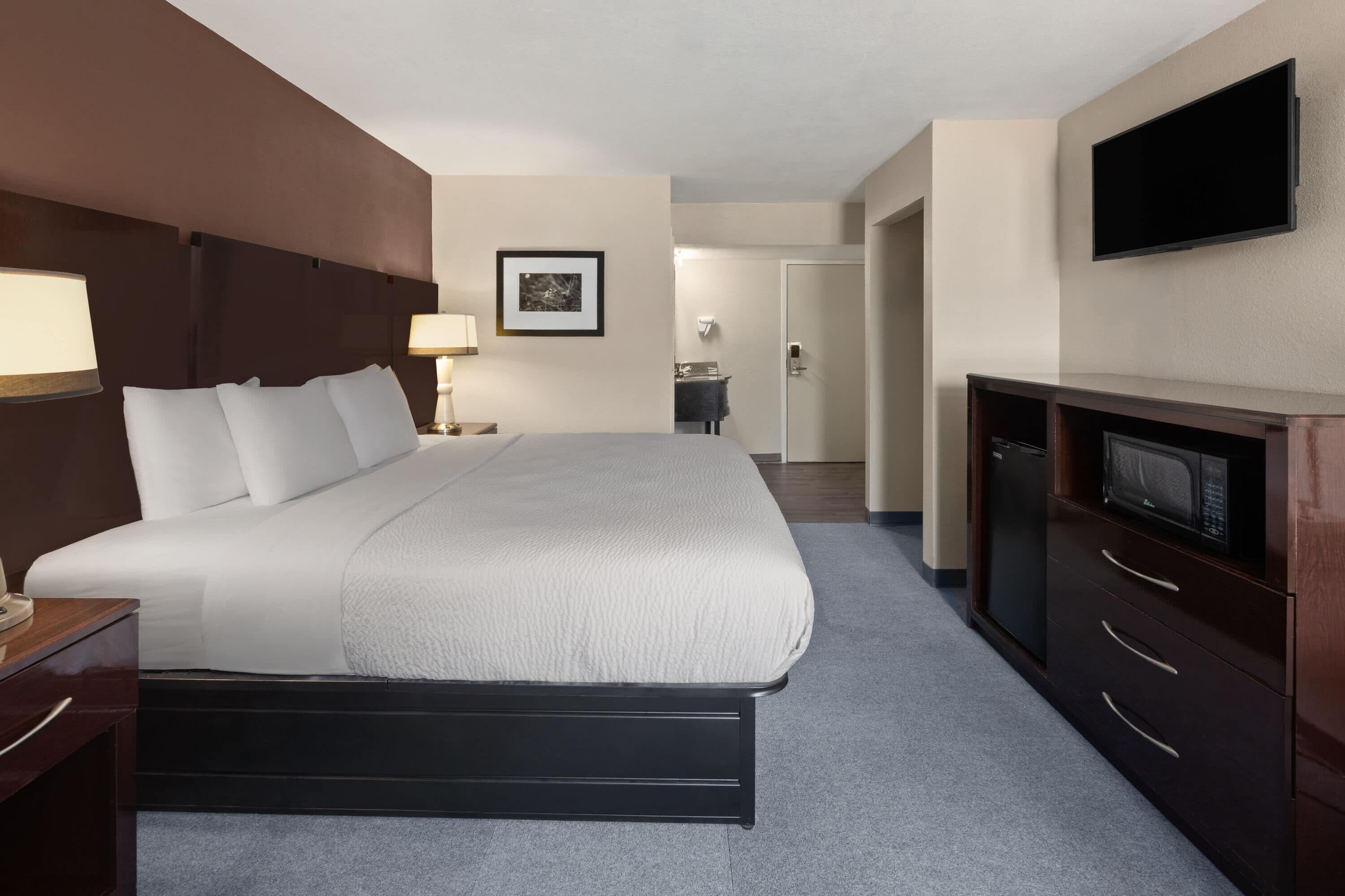 Una habitación de hotel con una cama grande, un escritorio con lámpara, televisión y un baño a la vista.