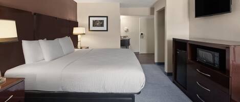 A hotel room with a large bed, a desk with a lamp, a television, and a bathroom visible in the background.