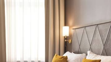 Habitación de hotel con cama, dos almohadas, mesita de noche, lámpara y cortinas traslúcidas.