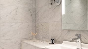Un baño moderno con pared de mármol, una bañera, un lavamanos y un espejo.