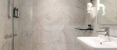 A bathroom with a marble floor, a glass shower enclosure, a white sink, and a mirror.