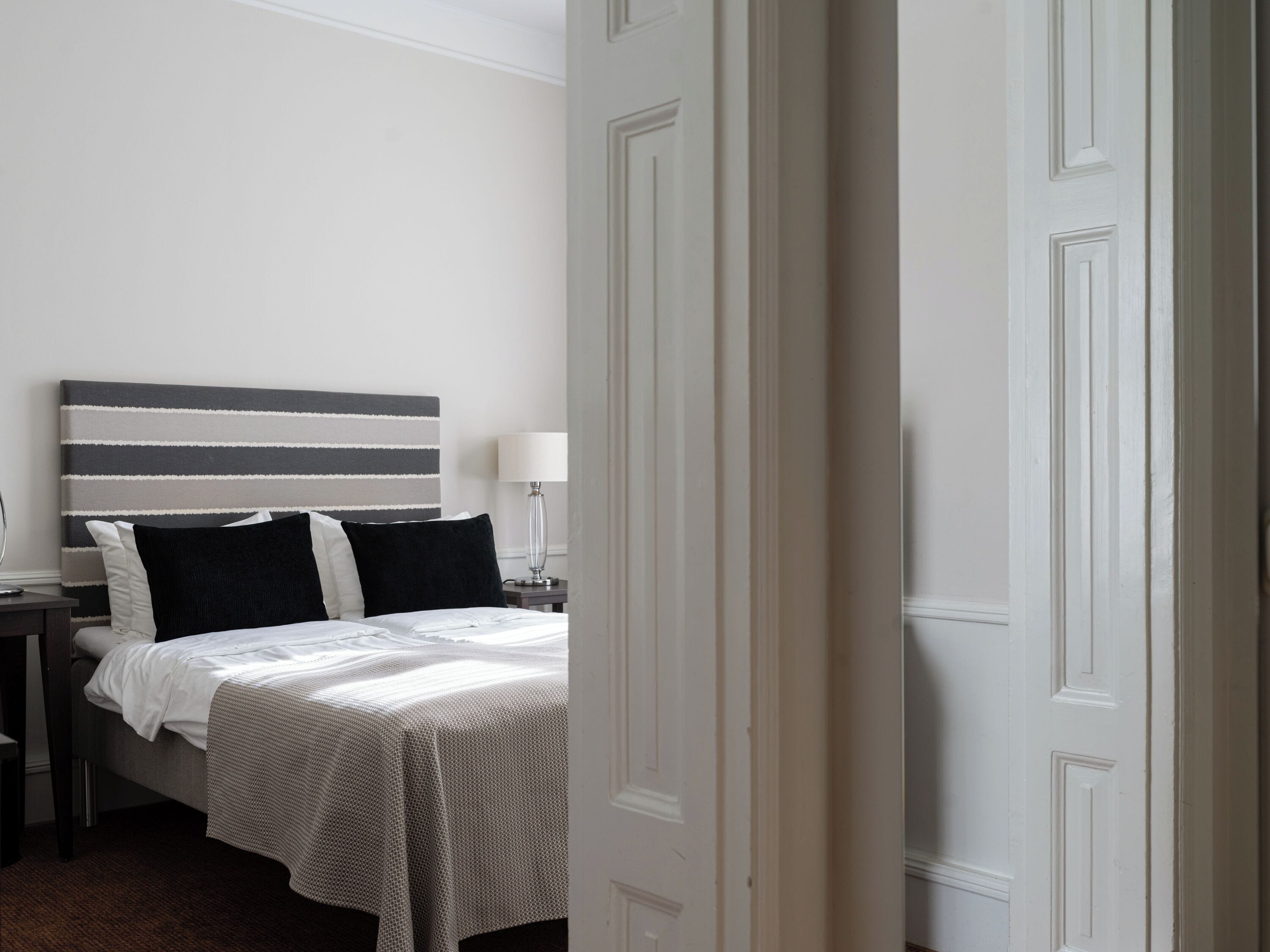 A hotel room with a bed, a nightstand, a lamp, and a door.