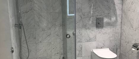 Ein modernes Badezimmer mit einer Duschkabine aus Glas, einer Toilette und einem Boden aus Marmorplatten.