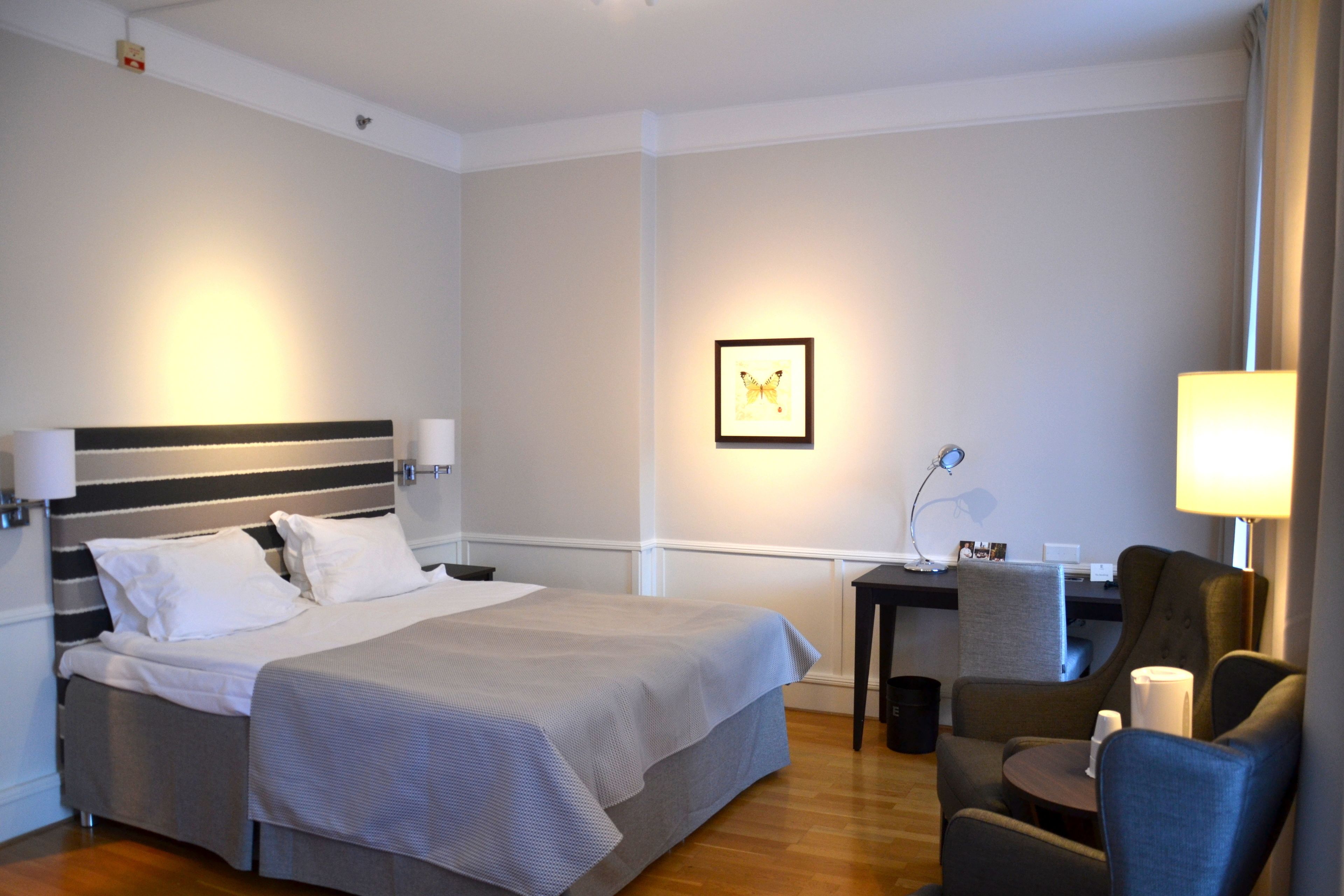 A hotel room with a large bed, a desk, a chair, and a small table.