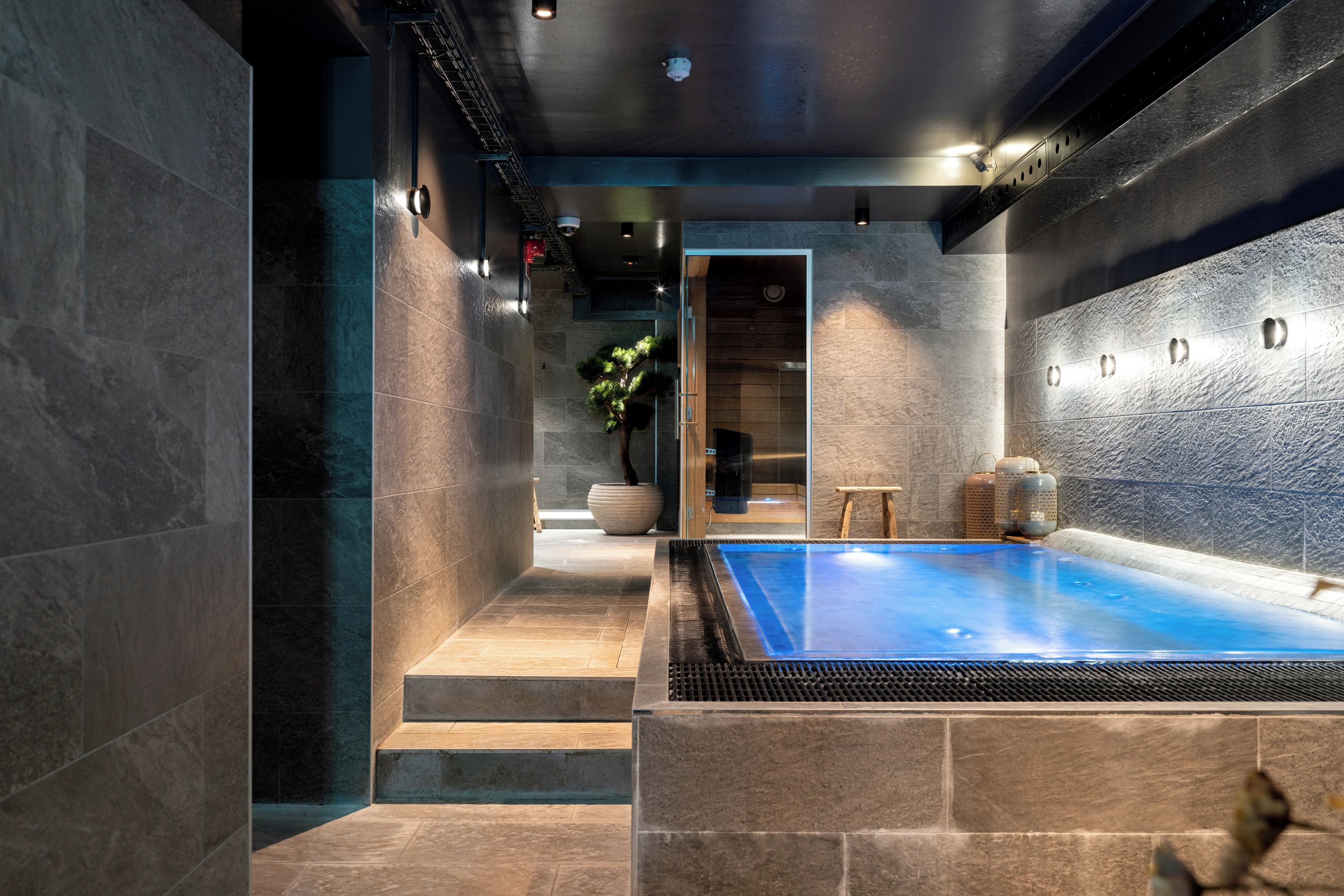 A modern spa area with a heated pool, stone walls, and a wooden bench.