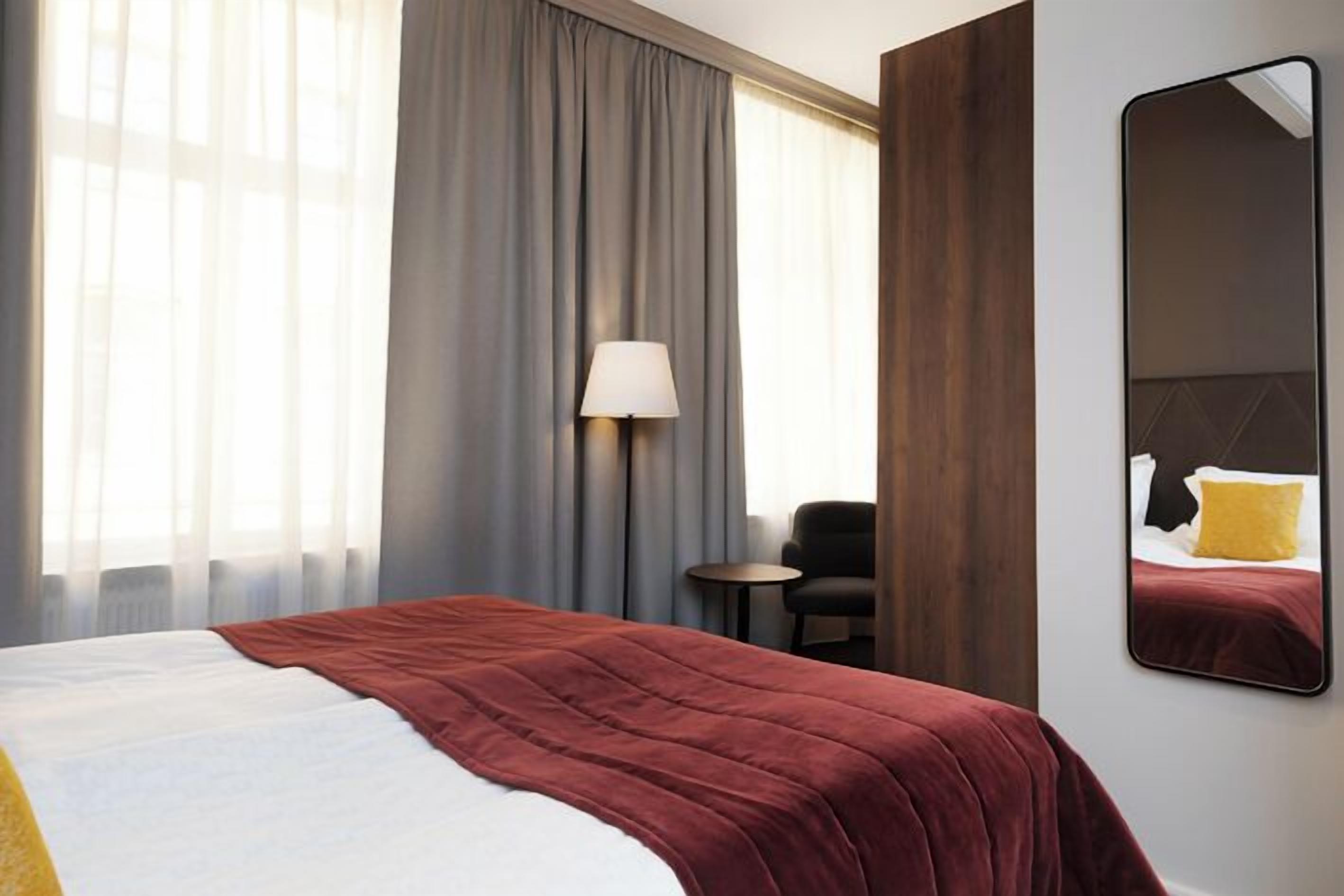 A hotel room with a large bed, a bedside lamp, a small table, and a mirror on the wall.