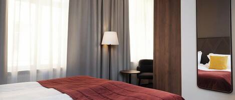 Habitación de hotel con una cama grande, una lámpara de noche, una mesita y un espejo en la pared.