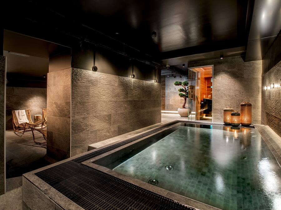 Een moderne spa met een groot rechthoekig zwembad, stenen muren en een zithoek met stoelen.
