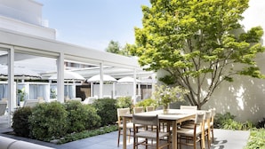 An outdoor patio with a wooden table and chairs, surrounded by greenery and umbrellas. - Graduate by Hilton Dallas (Dallas)