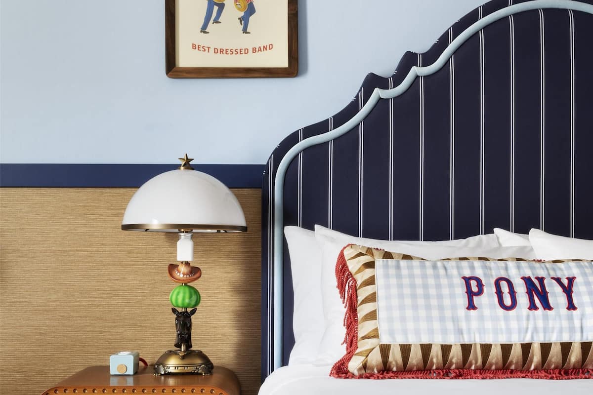A neatly arranged bedroom with a striped headboard, a framed picture of a band, a vintage radio, and a pillow with the word "PONY".