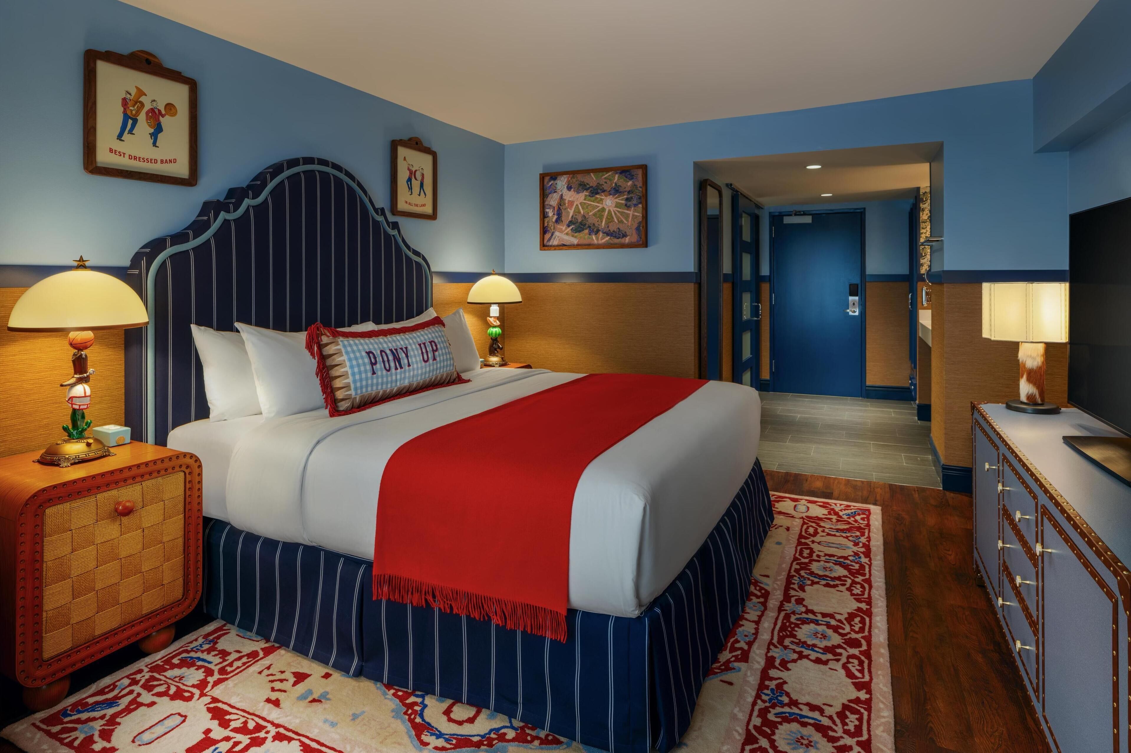 Una habitación de hotel con una cama grande, dos lámparas de noche, una mesita de noche de madera, un televisor y una puerta azul que da a otra habitación.