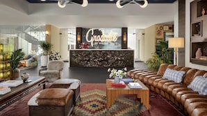 A modern hotel lobby with a reception desk, leather sofas, a patterned rug, and a large wall-mounted sign. - Graduate by Hilton Dallas (Dallas)