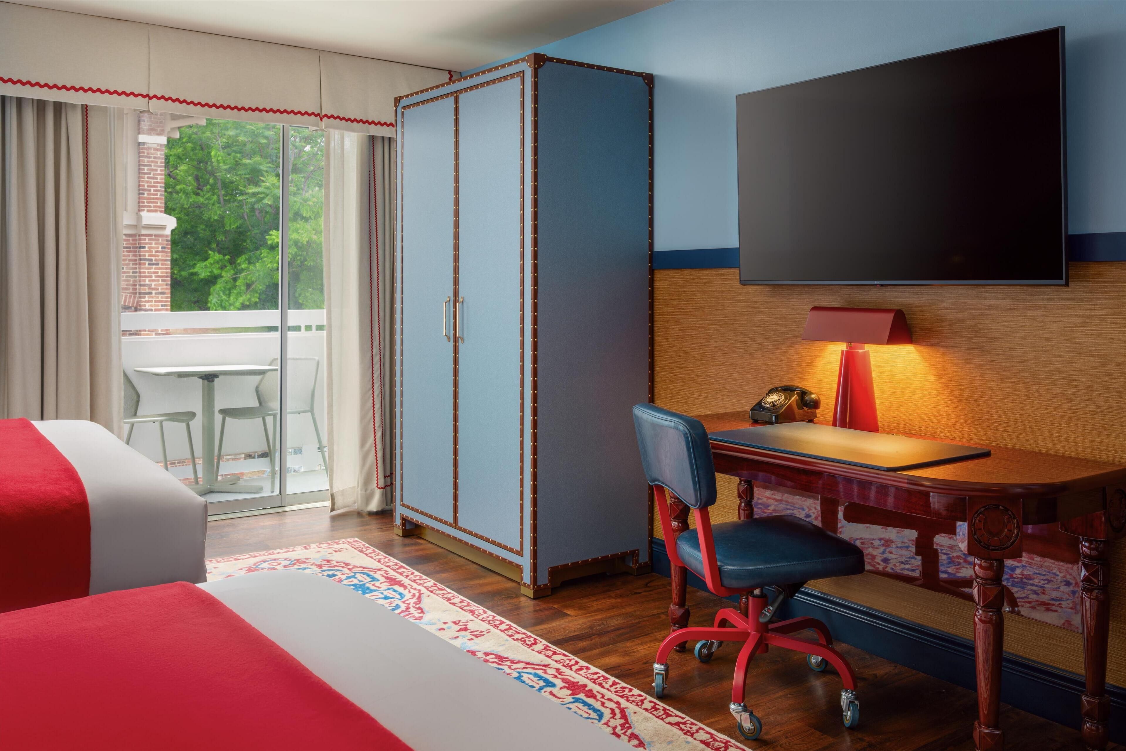 A hotel room with a bed, a desk with a chair, a television, and a wardrobe.