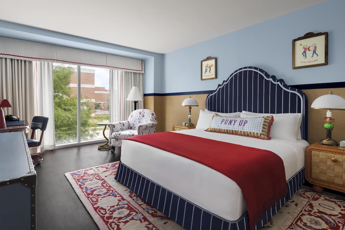 A hotel room with a large bed, a chair, a desk, and a view of the outdoors.
