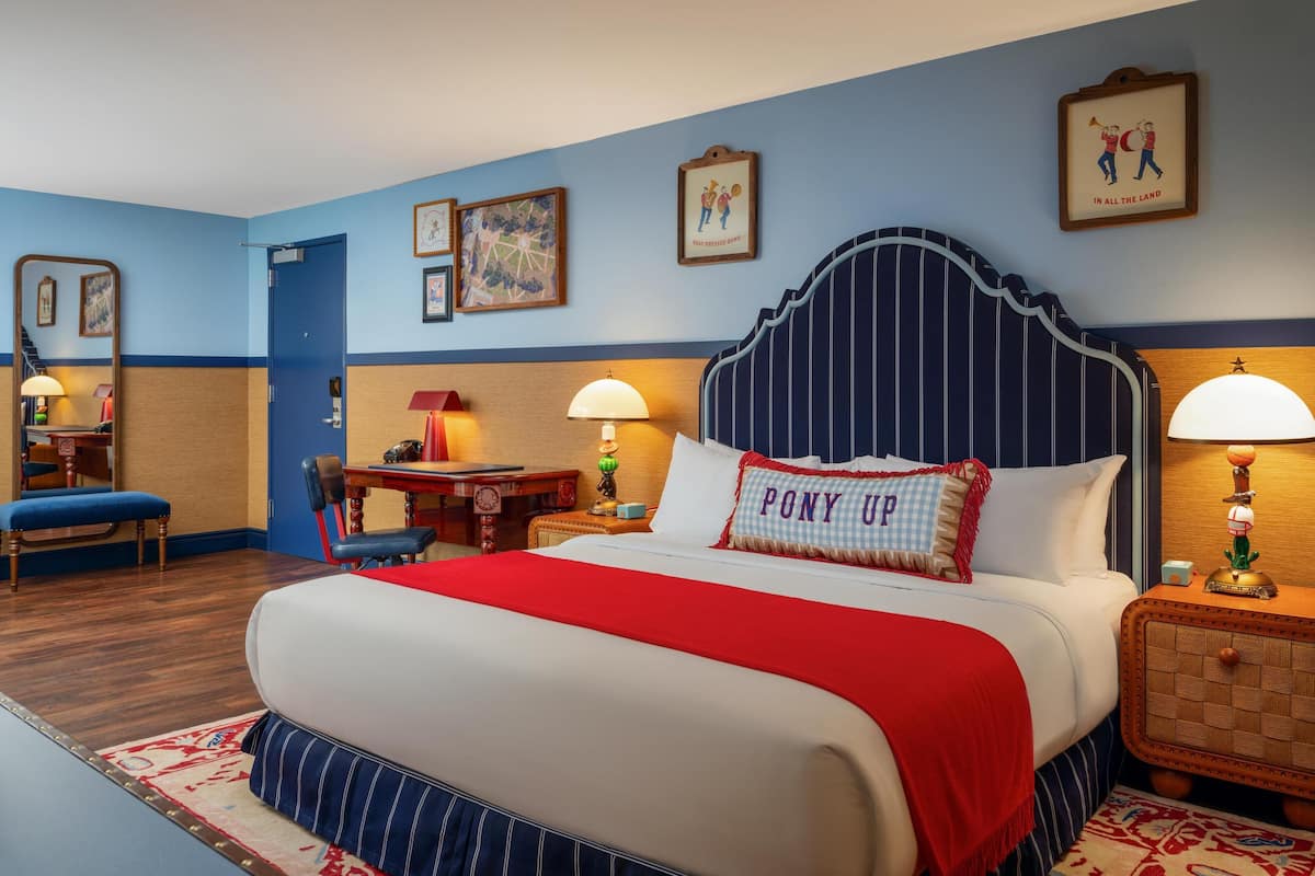 A hotel room with a large bed, a desk, a chair, and a small table.