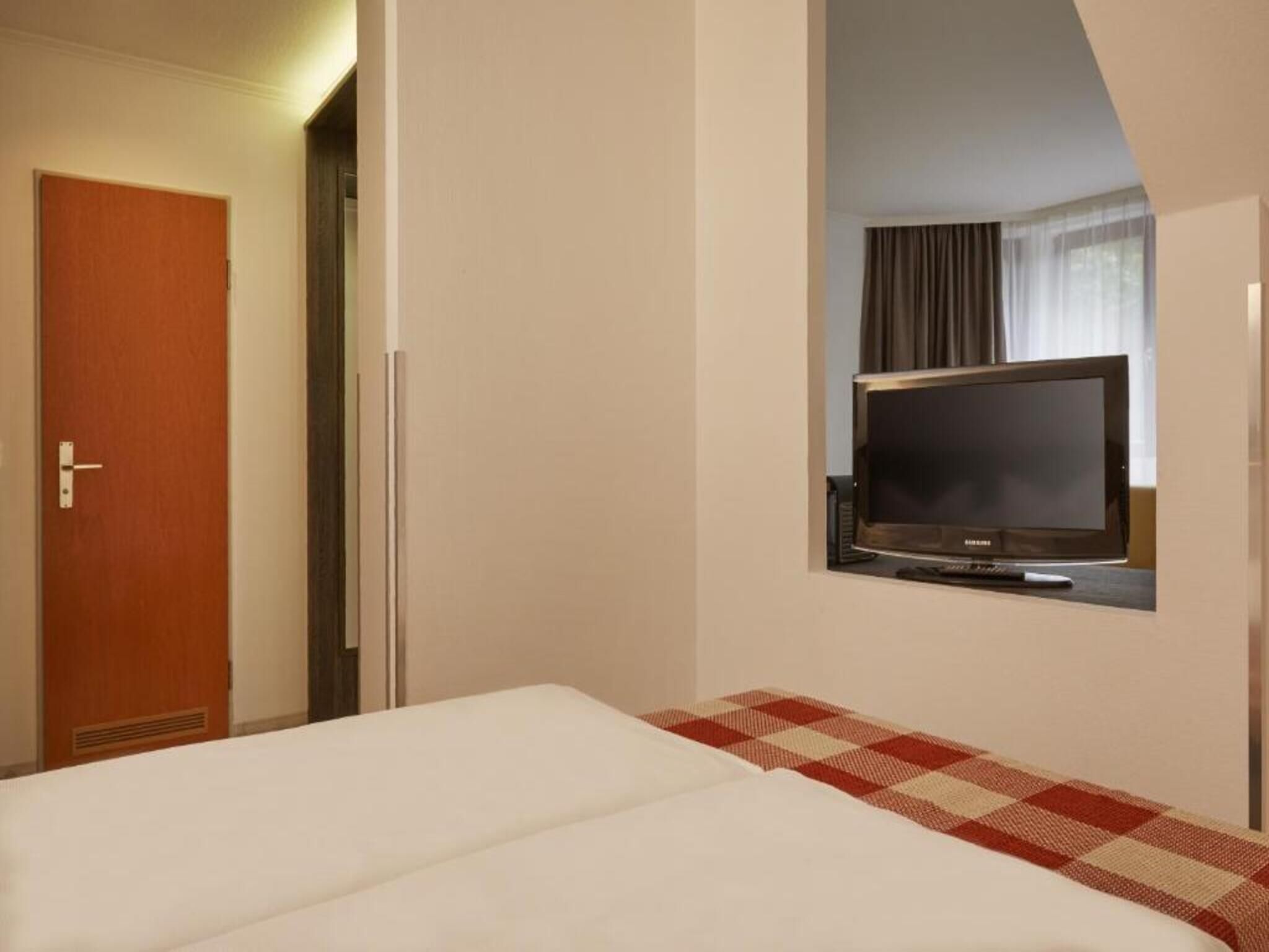 A hotel room with a bed, a television mounted on the wall, and a door.