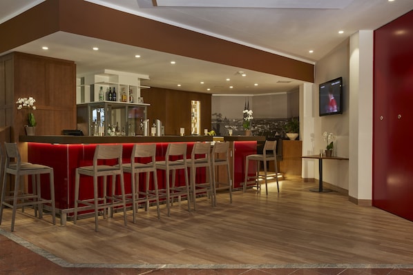 Zona de bar moderna con mostrador rojo, varios taburetes y vistas a la ciudad a través del ventanal.