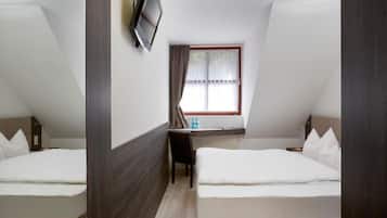 Habitación de hotel con dos camas, un escritorio, televisión y ventana con cortinas.