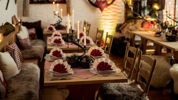 Un rincón comedor acogedor con mesas de madera dispuestas para una comida, velas y decoración rústica.