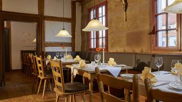 A dining area with wooden tables and chairs, white tablecloths, and hanging pendant lights.