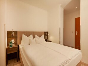 Una habitación de hotel con una cama grande, una mesita de noche con lámpara y un cabecero de madera.
