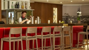 Una zona de bar con un cantinero, mostrador rojo y sillas de madera.